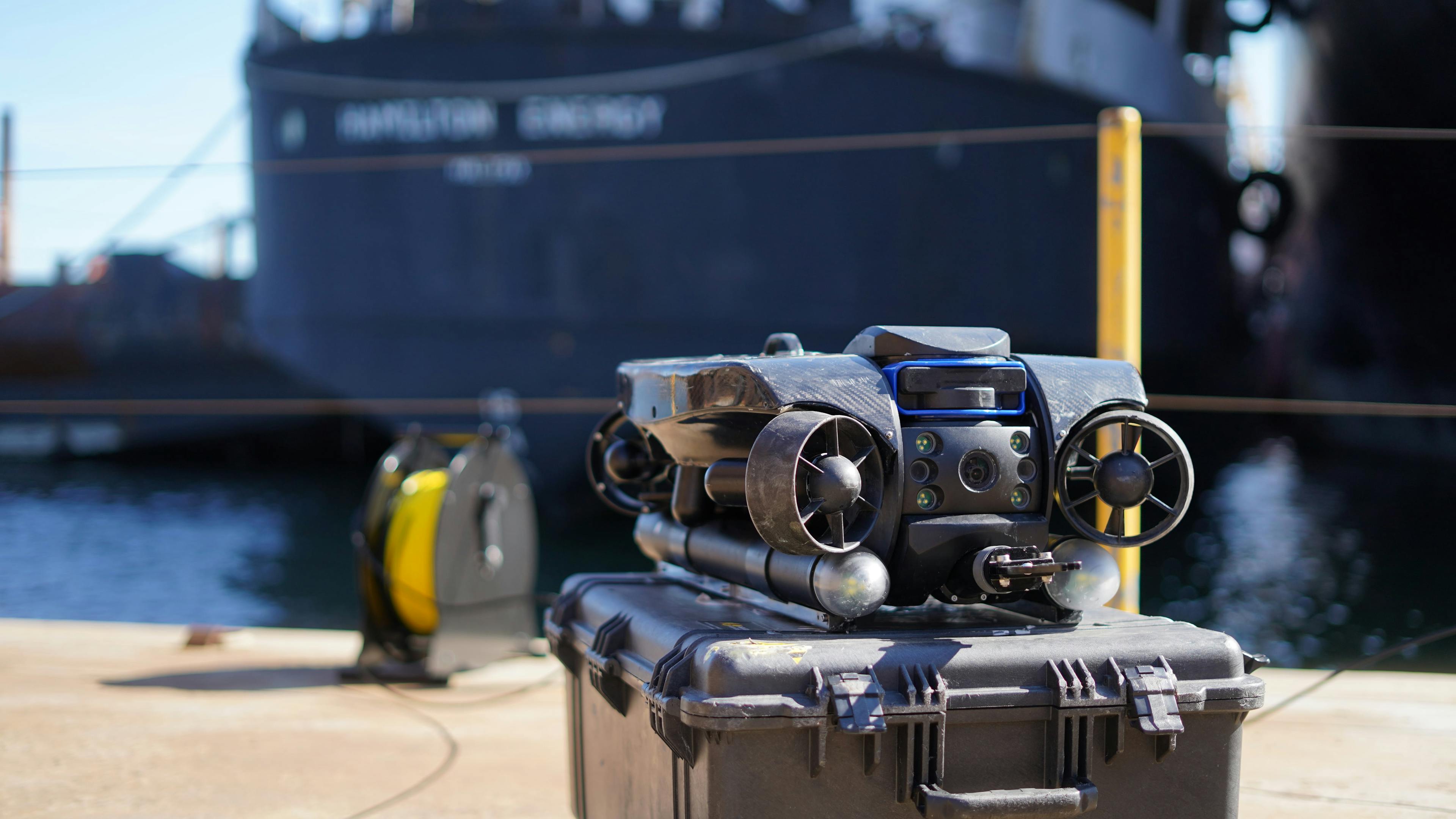 The Deep Trekker REVOLUTION ROV placed on a black box on a dock in front of a big blue ship 