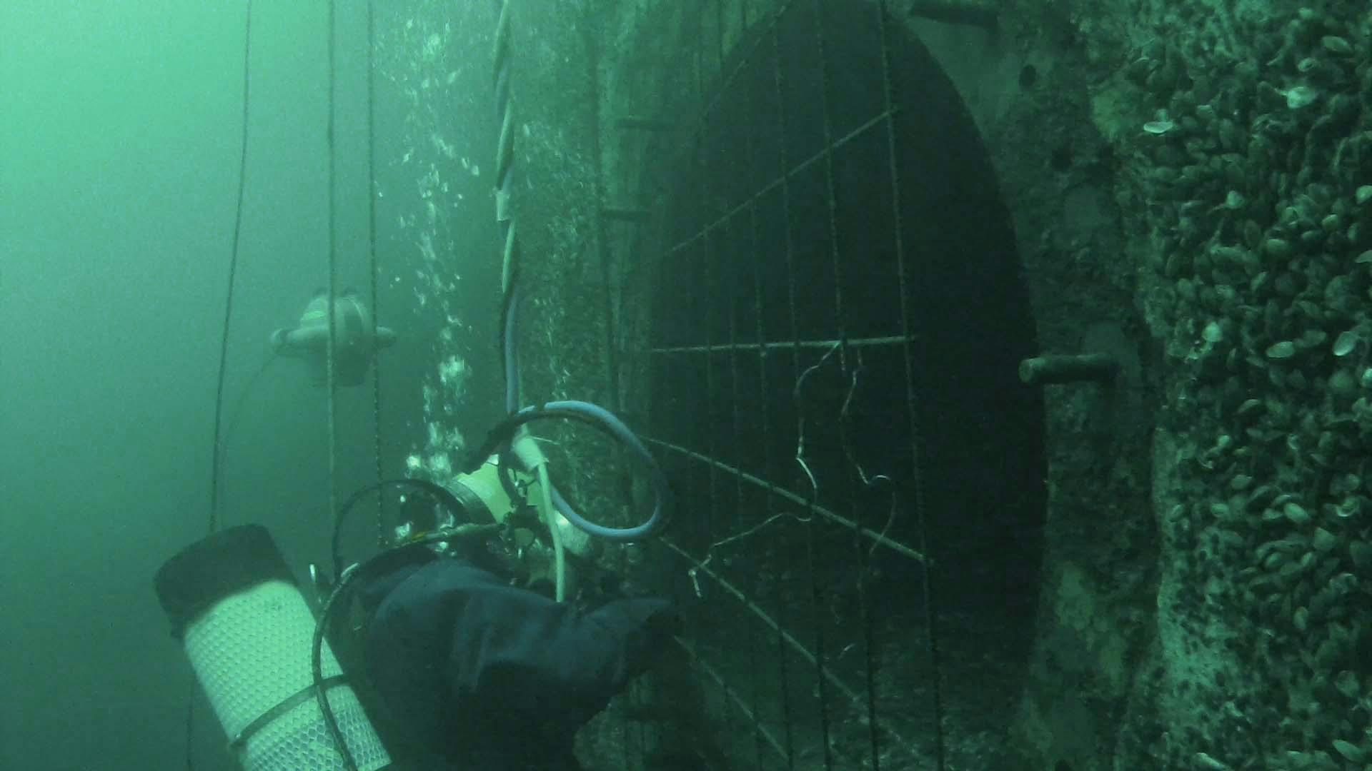 Scuba diver underwater at grate with DTG3 underwater ROV swimming behind diver. 