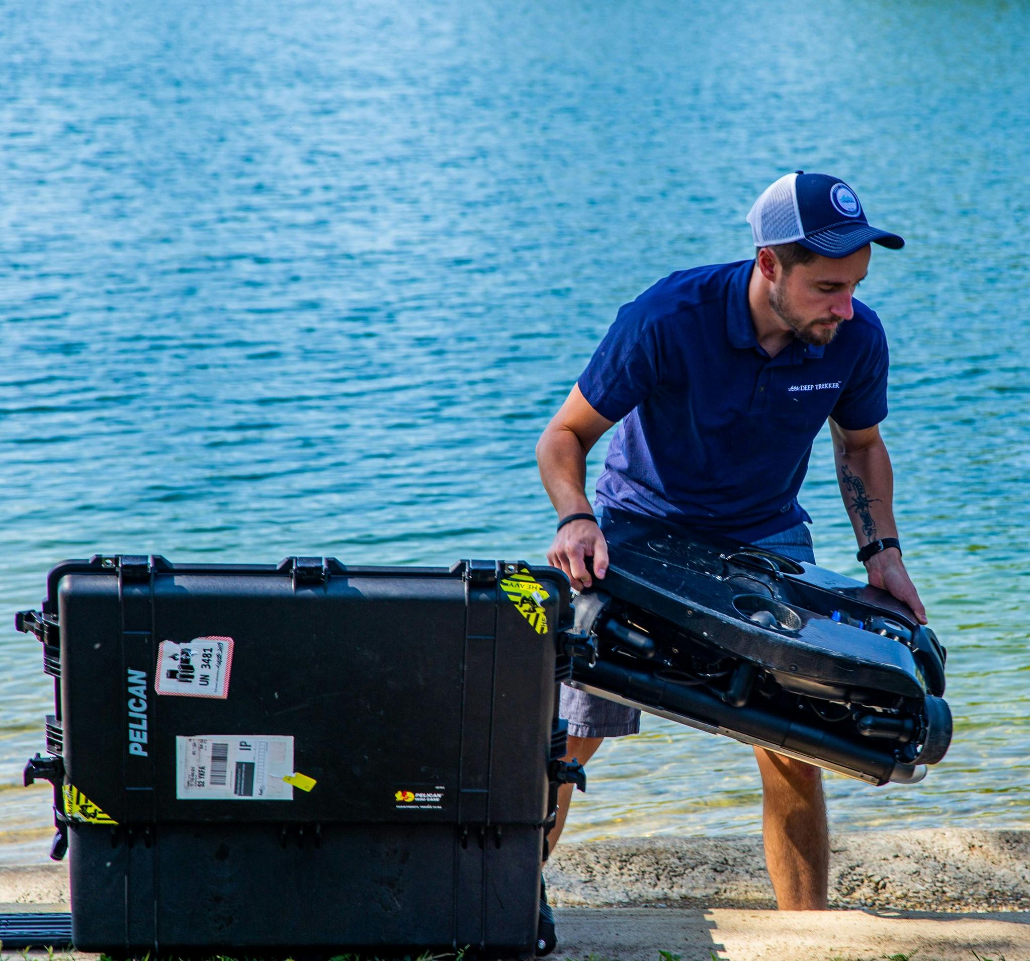 Man standing on shore lifting Deep Trekker REVOLUTION ROV out of the carrying case and into the water. 