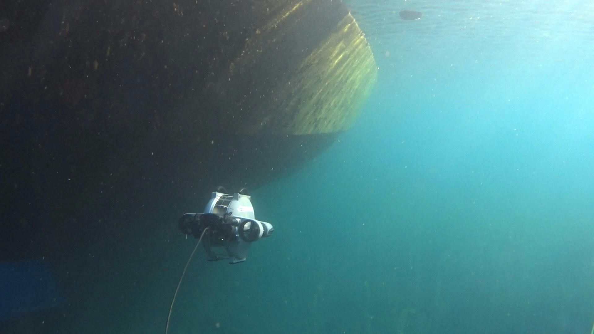 Deep Trekker DTG3 underwater ROV swimming in the ocean towards a large grey boat propeller. 