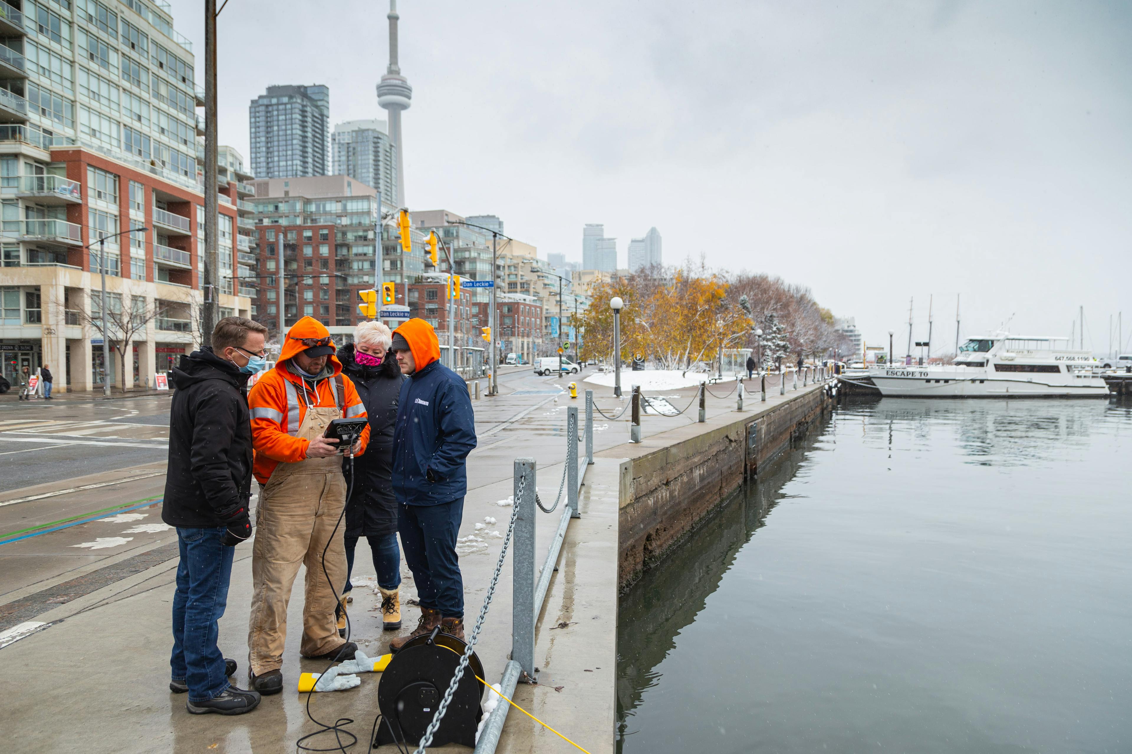 Group of employees standing along the shore in downtown Toronto looking at the controller of a Deep Trekker ROV.